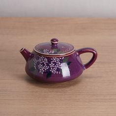 a purple tea pot with flowers painted on the side and lid sitting on a wooden table