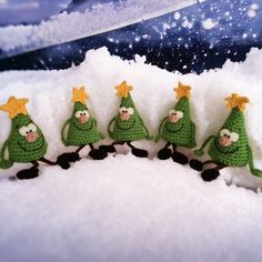 small crocheted christmas trees are lined up in the snow with gold stars on their heads