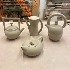 three teapots are sitting on a table in front of some other pottery items