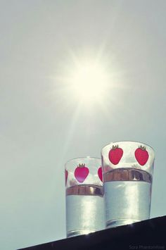 two shot glasses with strawberries on them sitting on top of a roof in front of the sun