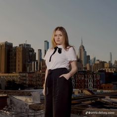 a woman standing on top of a roof with her hands in her pockets and looking at the camera