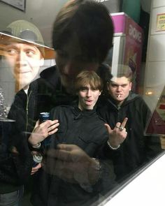 two young men standing next to each other in front of a window with posters on it