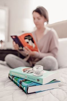 a woman sitting on her bed reading a book and looking at the books she is holding