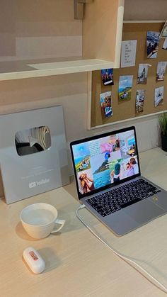 an open laptop computer sitting on top of a wooden desk next to a mouse and cup