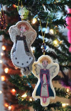 an ornament hanging from the christmas tree with two angel ornaments in front of it