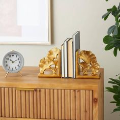 an alarm clock, books and plant on a wooden cabinet in front of a white wall