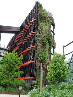 a very tall building with some plants growing on it's side and stairs going up the side