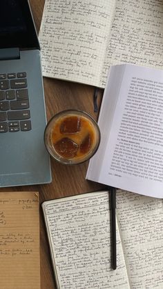 an open book sitting on top of a wooden table next to a cup of liquid