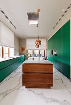 a kitchen with green cabinets and marble counter tops, along with an island in the middle