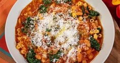 a white bowl filled with pasta and spinach on top of a colorful table cloth