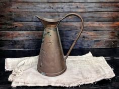 an old metal pitcher sitting on top of a white cloth next to a wooden wall