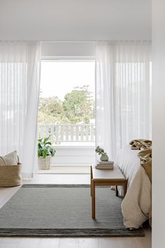 a bedroom with white drapes and curtains on the windowsill, along with a gray rug