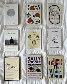 there are many different books on the bed with white sheets in this photo, all lined up together