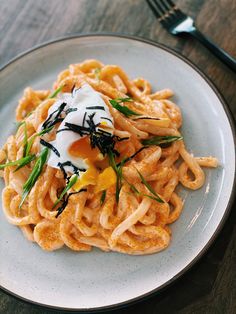 a white plate topped with pasta covered in sauce and an egg on top of it