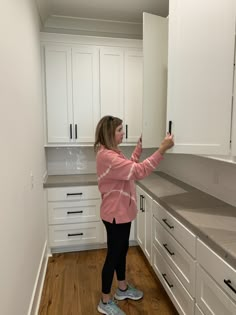 a woman standing in a kitchen next to white cabinets and cupboards with drawers on each side