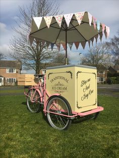 an ice cream cart is parked in the grass with a pink bicycle and canopy over it