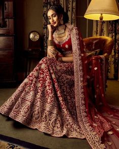 a woman in a red and gold lehenga sitting on a chair with lights behind her