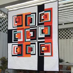 a quilt hanging from the side of a white fence next to a potted plant