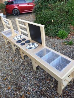 a wooden bench with three bowls and two trays on the back, in front of a red car