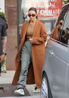 a woman in brown coat and pants stepping out of a car