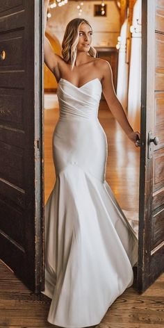 a woman in a white dress is standing at an open door and posing for the camera