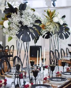 the table is set with black and white plates, silverware, and flowers in tall vases