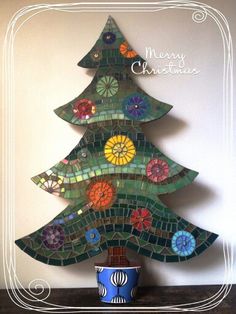 a christmas tree made out of stained glass tiles on a table with a blue and white vase