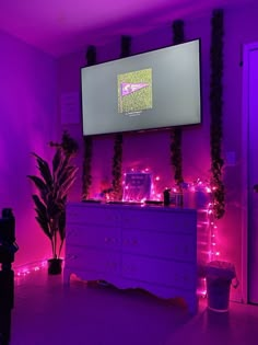 a room with purple lighting and plants on the wall, including a large television screen