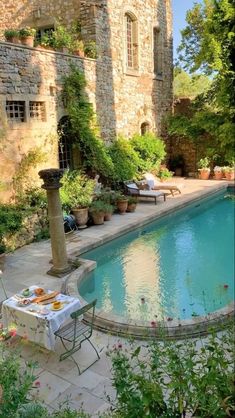 an outdoor swimming pool surrounded by greenery and stone walls, with chairs around it