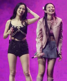 two young women standing next to each other on top of a purple stage holding microphones