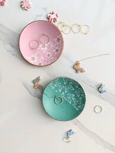 two pink and green plates sitting on top of a white table next to gold rings