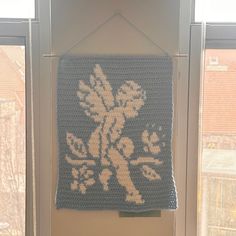 a crocheted blanket hanging on the wall in front of a window with an image of a bird