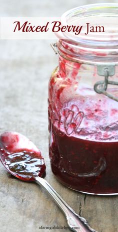 a jar filled with mixed berry jam next to a spoon on top of a table