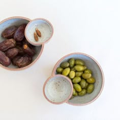 three bowls filled with different types of olives and nuts on a white table top