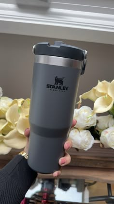 a person holding up a travel mug with flowers in the background