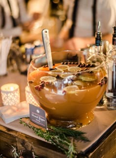 a table topped with a large bowl filled with liquid next to candles and bottles on top of it