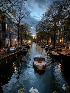 a boat traveling down a river next to tall buildings and trees in the evening time