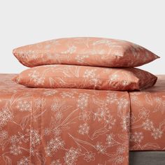 two pillows are stacked on top of each other in front of a bed with an orange floral print