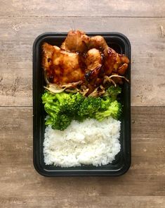 a tray with rice, broccoli and chicken on it sitting on top of a wooden table