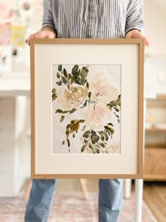 a person holding up a framed painting with flowers on it