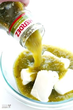 someone pouring sauce into a glass bowl filled with food