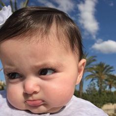 a close up of a baby wearing a white shirt with a flower in it's hair