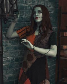 a woman dressed up as a skeleton holding a lantern in her hand and standing next to a brick wall