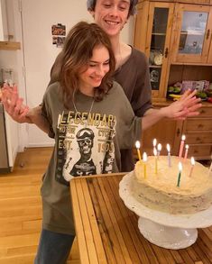 two people standing in front of a cake with lit candles