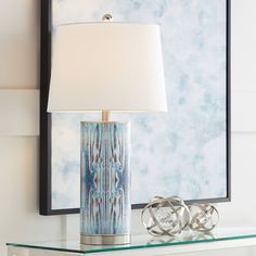 a table lamp sitting on top of a glass shelf next to a framed art piece