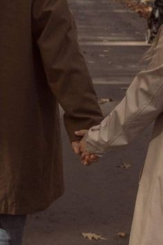 two people holding hands while walking down the street