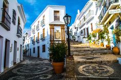 an alleyway with white buildings and cobblestone streets in the city center, surrounded by potted plants