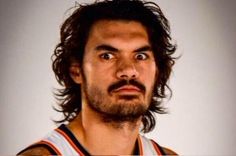 a man with long hair and beard wearing a basketball uniform looking up at the camera