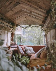 a couch sitting under a wooden roof next to a window filled with plants and greenery