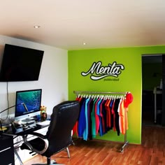 a room with a desk, chair and computer on the wall that has neon colored shirts hanging in front of it